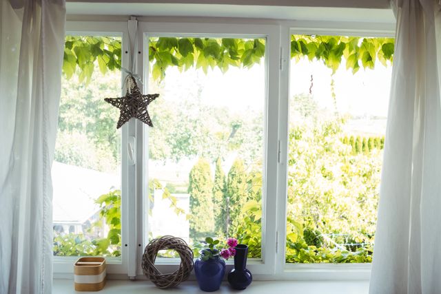 Wicker star hanging on window with lush garden view, creating a cozy and peaceful home atmosphere. Ideal for articles or blogs about home decor, interior design, and creating a serene living space. Perfect for promoting home decor products or illustrating concepts of natural light and greenery in homes.