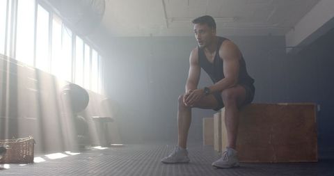Man resting on box in gym with sunlight streaming