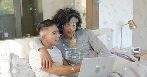 Couple relaxing in bed sharing laptop with holographic digital network overlay