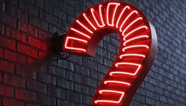 Glowing red neon question mark bathing brick wall, urban night signage and reflections