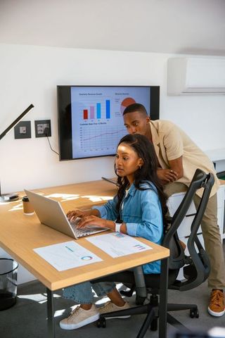 Coworkers Analyzing Quarterly Data on Laptop and Monitor in Office