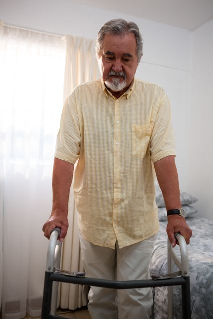 Senior man walking with walker in bedroom at nursing home