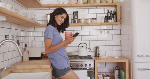 Relaxed woman using smartphone in white tile kitchen