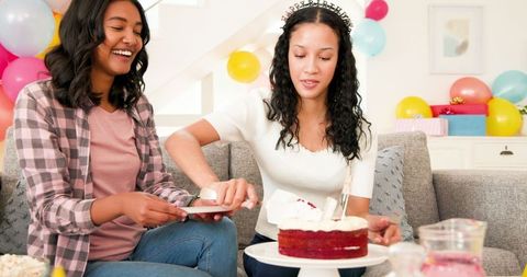 Two Women Celebrating Birthday on Sofa with Cake and Balloons