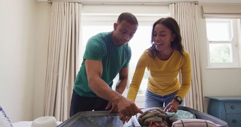 Smiling biracial couple packing suitcase for exciting holiday travel