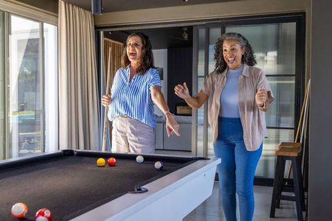 Women celebrating pool win, pointing and laughing by black-felt billiards table