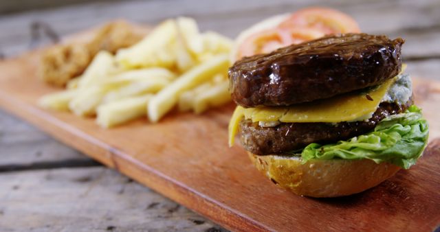 A juicy double cheeseburger is served on a wooden board with a side of fries and onion rings, showcasing a classic American fast food meal. Its presentation on the rustic surface enhances the appeal of this indulgent and popular dish.