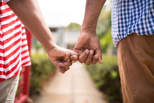 Cropped image of senior couple holding little fingers while standing in yard