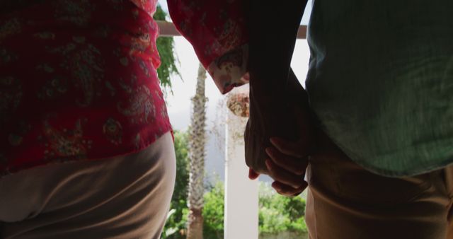 Mid section of senior african american couple walking holding hands in garden with copy space. Senior lifestyle, retirement and domestic life concept, unaltered.
