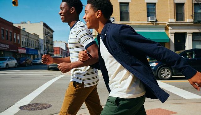 Two black teens walking and laughing while crossing urban neighborhood intersection