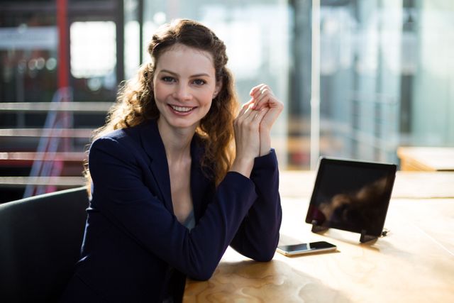 Businesswoman sitting at desk in modern office, smiling confidently. Ideal for corporate websites, business presentations, career-related articles, and professional networking profiles.