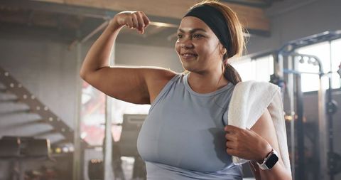 Confident woman flexing bicep post workout in gym representing strength fitness positivity