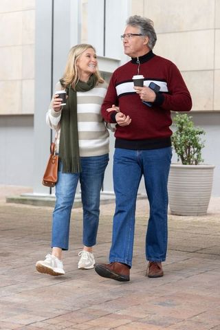 Mature couple walking arm-in-arm enjoying coffee and conversation in urban plaza