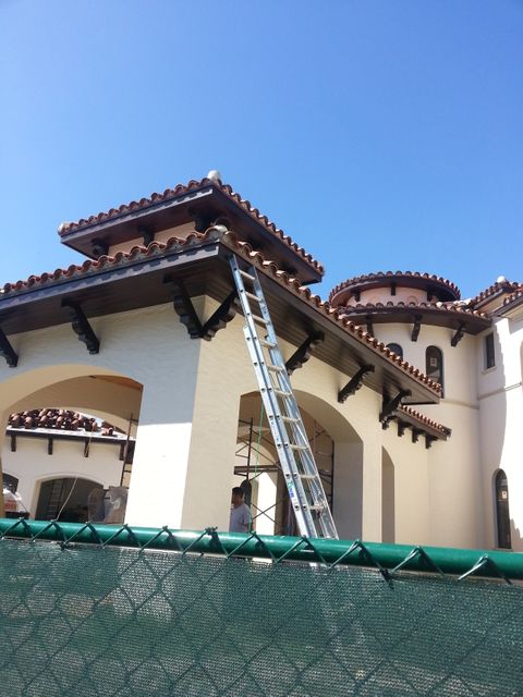 Mediterranean style villa under construction with ladder against cream walls and green fence in foreground. This visual is suitable for real estate development promotions, architecture portfolios, or showcasing residential construction projects.