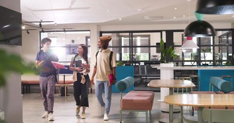 African american students walking, chatting and collaborating in modern campus lounge holding tablet