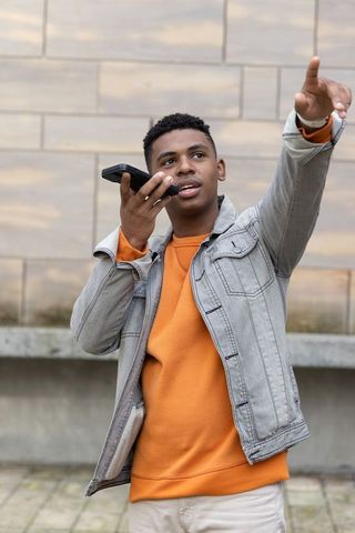 Young african american teen speaking into smartphone pointing forward in urban plaza