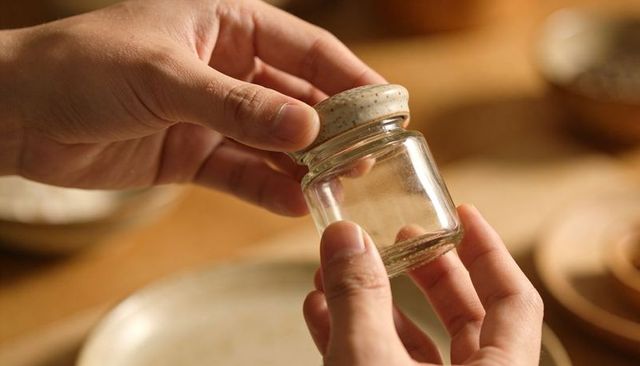 Holding small glass jar with speckled ceramic lid on wooden table