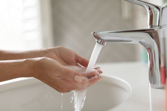 Close-up of woman washing her hands in washbasin in bathroom