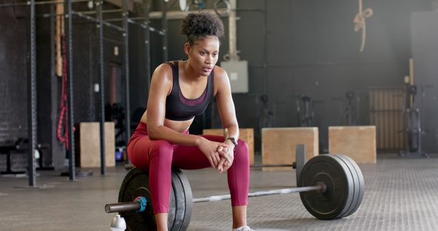 Exhausted biracial sportswoman resting on weight bar and sweating at gym - Download Free Stock Photos Pikwizard.com