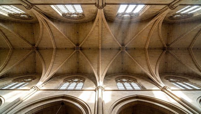Sunlight streaming through clerestory onto gothic ribbed vaults and pointed arches