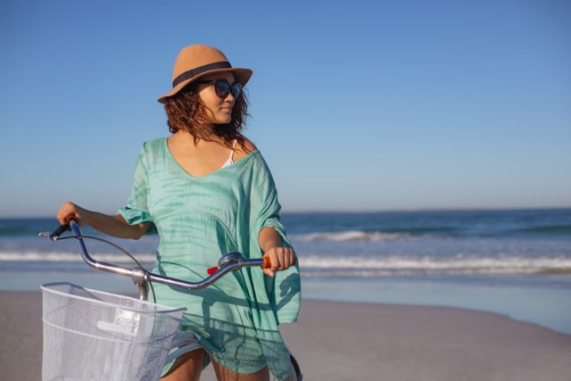 Woman enjoying a sunny day at the beach with her bicycle. Ideal for use in travel brochures, summer vacation promotions, lifestyle blogs, and advertisements focusing on outdoor activities and relaxation.