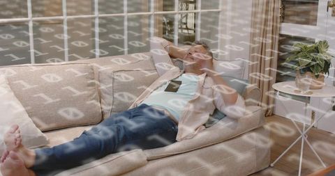 Mature man relaxing on sofa with smartphone on chest and digital binary overlay