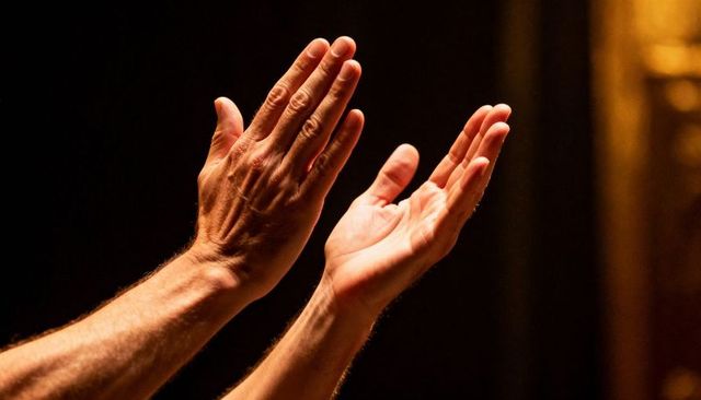 Applauding hands catching warm spotlight on theater stage with dramatic chiaroscuro