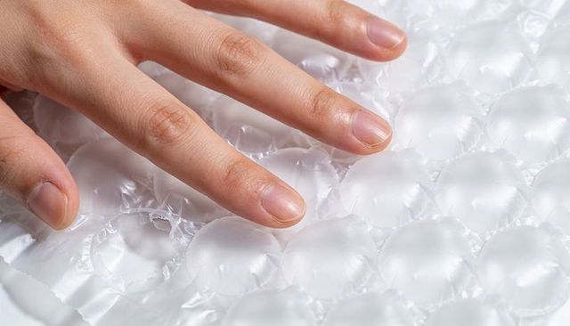 Fingertips pressing bubble wrap with popped bubbles for stress relief and texture close-up
