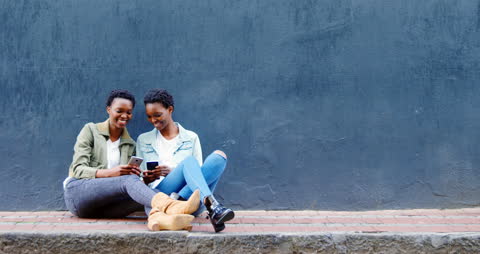 Twin Sisters Enjoying Smartphones on Urban Sidewalk