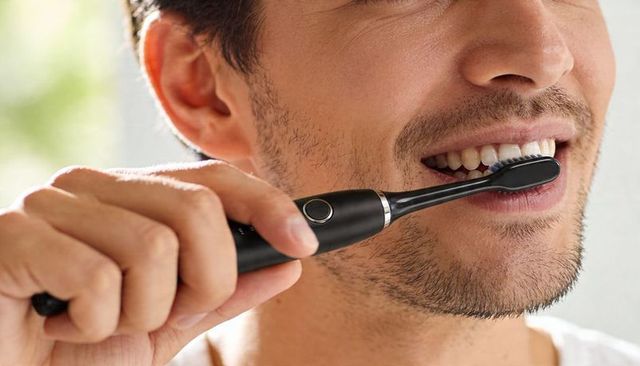 Closeup man brushing teeth with black electric toothbrush near window in natural light