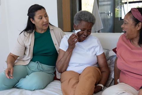 African american senior women laughing while using handheld wellness device on temple