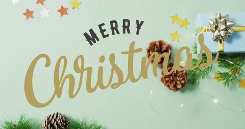 Merry Christmas gold script on mint tabletop featuring blue gift, pinecones, glitter stars