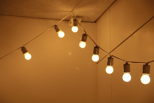 Warm string lights are hanging in a corner, providing a cozy and inviting glow. Perfect for creating an ambient atmosphere in homes, parties, or event setups. Suitable for use in promotional materials for interior design, event planning, or advertising cozy and inviting spaces.