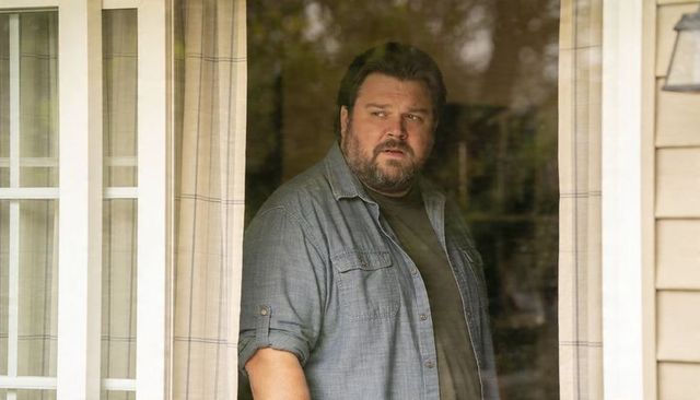 Thoughtful man looking through glass door at porch with denim shirt and window reflection
