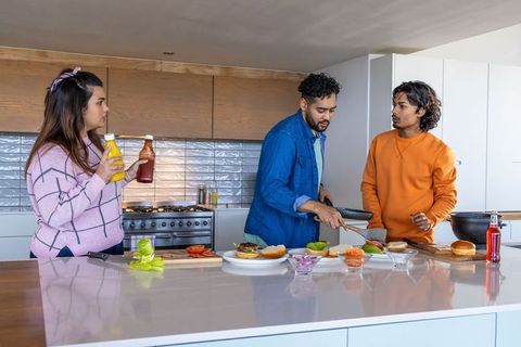 Friends assembling burgers at modern kitchen island passing ketchup and mustard