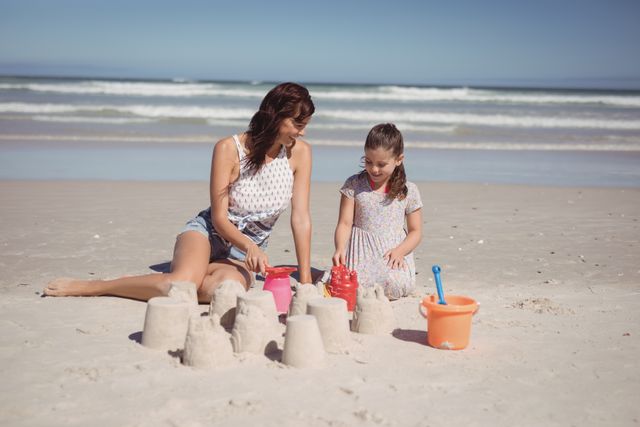 Happy girl with mother making sand castle at beach during sunny day