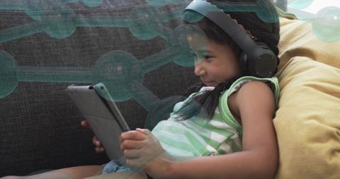 Girl relaxing with tablet and headphones on sofa, concentrating with digital learning overlay