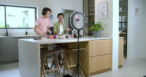 Multiracial friends filming and preparing recipe on modern kitchen island with ring light