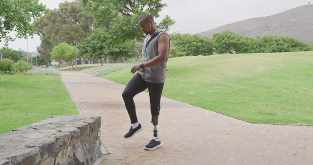 Energetic man with prosthetic leg exercising in a green park, demonstrating strength and resilience. He wears athletic clothing and sneakers, showing commitment to fitness and healthy living. Useful for themes on rehabilitation, health, motivation, and disability awareness.
