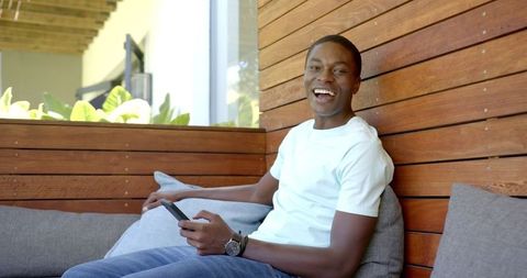 Happy Young Man Relaxing on Patio with Smartphone