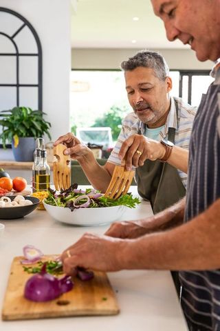 Senior Male Friends Enjoying Salad Preparation in Modern Kitchen