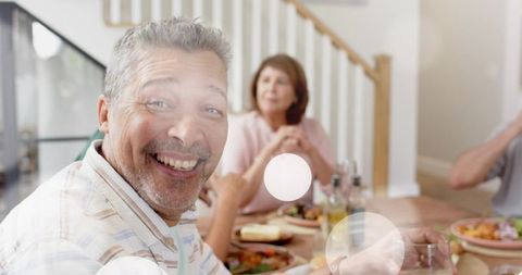 Smiling middle-aged man enjoying cozy family dinner at home with salad and drinks