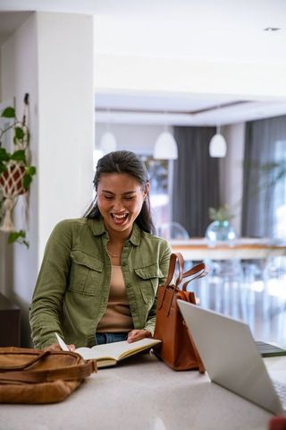 Asian woman taking notes smiling laptop modern lounge cafe