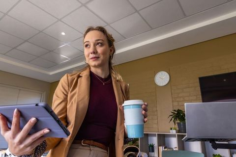 Professional woman presenting with tablet and reusable cup in minimalist office meeting