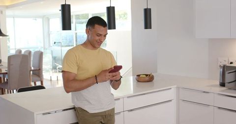Young man leaning on kitchen island checking smartphone, relaxed open-plan home lifestyle