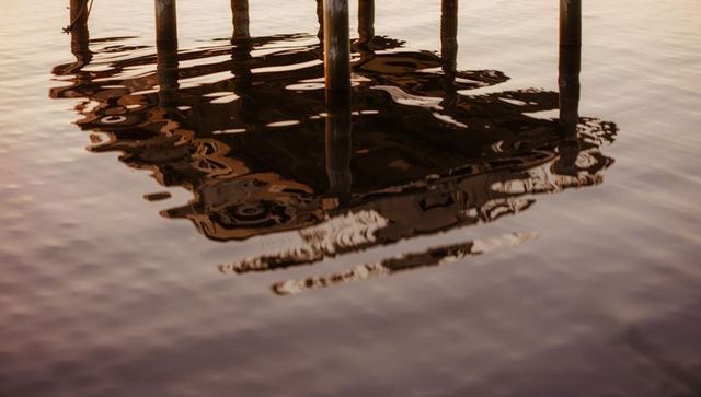 Sunlit wooden pier pilings reflecting on rippled lake water at sunset