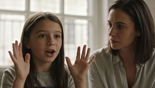 Preteen girl talking and gesturing while mother listens in sunlit living room