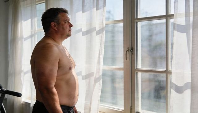 Midlife man gazing out sunlit window in home gym, reflecting on fitness goals and wellness