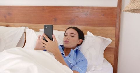 Woman in Light Blue Pajamas Using Smartphone in Cozy Bedroom