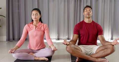 Couple meditating at home in lotus pose on yoga mats practicing mindfulness and breathing